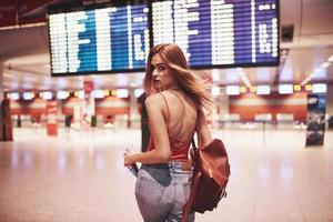 belle jeune fille touristique avec sac à dos à l'aéroport international, près du panneau d'information sur les vols photo
