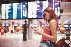 belle jeune fille touristique avec sac à dos à l'aéroport international, près du panneau d'information sur les vols photo
