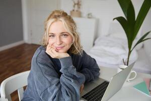 portrait de Jeune souriant femme, femelle étudiant séance dans sa pièce avec ordinateur portable, à la recherche mignonne à caméra photo