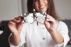 souriant et de bonne humeur. femme médecin montrant le petit phoropter en le tenant à deux mains photo