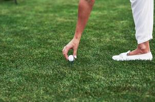conception de sport et de passe-temps. main féminine mettant une balle de golf sur la broche debout dans le champ vert photo