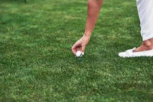 main féminine mettant une balle de golf sur la broche debout dans le champ vert photo