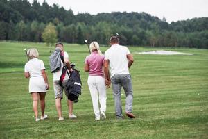 groupe de quatre amis portant du matériel de golf allant au prochain point du terrain photo