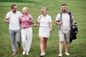 marcher sur la pelouse. amis joyeux passant du temps sur le terrain de golf avec des bâtons et de la bonne humeur photo