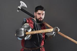 chevalier médiéval sur fond gris. portrait d'un guerrier brutal au visage sale avec une armure de cotte de mailles, des vêtements rouges et noirs et une hache de combat photo