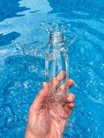 main éclabousser l'eau de clair verre bouteille dans une bleu piscine, dynamique mouvement Geler tir. nettoyer l'eau concept. photo