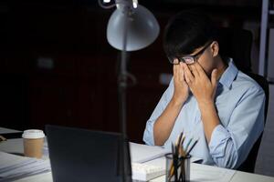 homme d'affaire travail heures supplémentaires à le sien Bureau fait du le sien yeux fatigué. photo