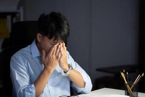 homme d'affaire travail heures supplémentaires à le sien Bureau fait du le sien yeux fatigué. photo