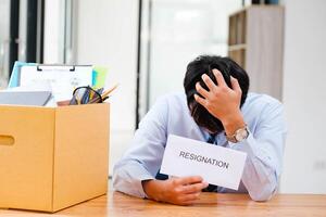 homme à bureau avec démission lettre, méditer le sien décision à côté de une emballé boîte. photo