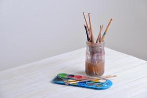 pot avec brosses et aquarelles sur en bois tableau. génial pour Créatif projets ou artistique thèmes photo