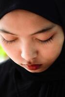 proche en haut de le visage de une magnifique Javanais femme portant une noir foulard. photo