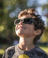 une Jeune garçon portant protecteur des lunettes est en train de regarder le solaire éclipse. photo