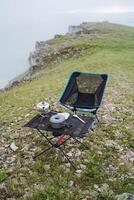 une ensemble de touristique ustensiles pour camping dans nature, pliant meubles sur une randonnée, une pot avec une couvercle, une Cadre table pour déjeuner, une Montagne paysage. photo