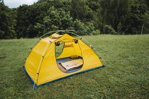 une Jaune tente pour randonnée des stands sur le herbe dans le forêt, camping équipement pour en train de dormir dans nature, une endroit à repos, une Cadre de aluminium arches camping dans le montagnes. photo