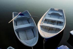 deux bateaux supporter sur le l'eau lié à le jetée, plaisir bateaux sur le lac, aviron avirons, une gris navire, une silencieux port. photo