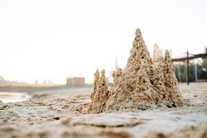 le sable Château sur le mer plage, enfants amusement à jouer avec humide sable, le sable tours contre le Contexte de le soleil, Matin Aube sur le mer, côte vacances photo