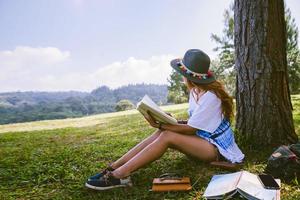 femme asiatique voyage nature. voyage se détendre. fille assise lisant un livre sous l'arbre. belle fille dans la forêt d'automne en lisant un livre d'éducation à la nature et en écrivant une note. photo