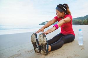 femmes asiatiques jogging séance d'entraînement sur la plage. asseyez-vous sur la plage fitness détendez-vous avec des jambes étirées et des bras étirés. photo