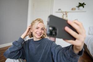 portrait de Jeune femme, social médias influenceur, prise selfies dans sa chambre, séance sur sol, en portant téléphone intelligent et posant pour une photo