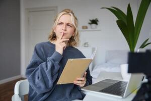 portrait de Jeune femme, étudiant séance dans chambre, en train d'étudier de maison, éloigné éducation concept, en portant carnet et pensée, à la recherche de côté avec réfléchi affronter, se concentrer sur affectation photo