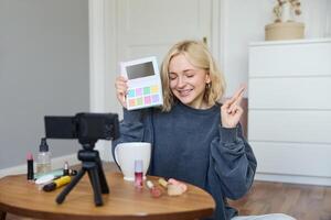 portrait de magnifique mode de vie blogueur, fille enregistrements une sur sa caméra pour social médias, spectacles palette de fards à paupières, Est-ce que une maquillage Didacticiel pour sa suiveurs, est assis dans sa pièce photo