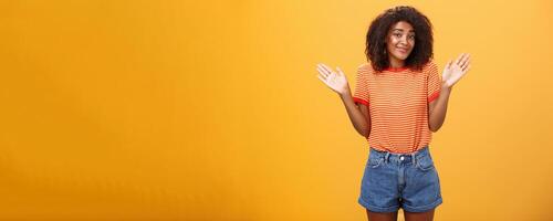 non idée faire ne pas se soucier. négligent et indifférent calme content africain américain femme avec frisé cheveux dans été vêtements élevage paumes et haussant les épaules dans non impliqué pose souriant insouciant étant ignorant photo