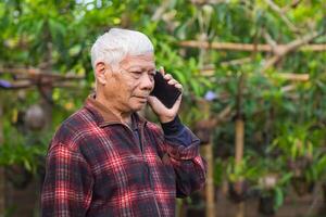 personnes âgées homme en utilisant une téléphone intelligent tandis que permanent dans une jardin. espace pour texte photo