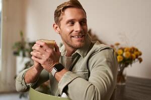 café, loisir et mode de vie concept. portrait de Beau Jeune homme est assis sur chaise avec verre de café, les boissons le sien boisson et souriant photo