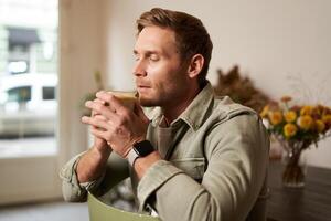 portrait de Beau blond homme dans café, est assis sur chaise, jouit le goût de délicieux fraîchement brassée tasse de café photo