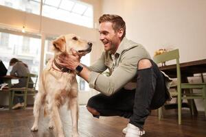 portrait de content Jeune homme entre dans café magasin avec le sien d'or retriever. Beau gars caresse chien dans acceptant les animaux café photo