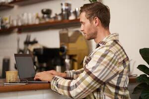 portrait de Jeune homme, numérique nomade travail sur projet, en utilisant portable dans café, en buvant café et dactylographie, navigation sur le l'Internet photo