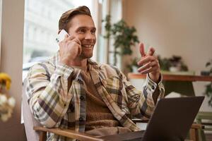 Beau homme d'affaire dans café boutique, séance dans café avec portable et appel quelqu'un, homme parlant sur le téléphone avec client, fabrication enquête à propos projet, parlant à collaborateur tandis que travail à distance photo