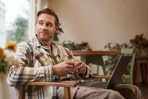 Beau Jeune professionnel, homme d'affaire séance dans café avec verre de café et travail sur ordinateur portable, recherche pour inspiration à l'extérieur de Bureau espace de travail photo