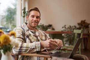 Beau Jeune professionnel, homme d'affaire séance dans café avec verre de café et travail sur ordinateur portable, recherche pour inspiration à l'extérieur de Bureau espace de travail photo