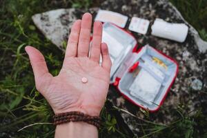 une rose tablette mensonges dans le main, premier aide pour empoisonnement dans une randonnée, une premier aide trousse pour urgence se soucier dans le forêt, touristique équipement, médecine, antibiotiques. photo