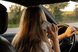 Jeune femme en utilisant mobile téléphone tandis que conduite voiture sur Autoroute route pendant le coucher du soleil. femmechauffeur a accident appel avec téléphone intelligent pour aider. affaires femme occupé conduite concept photo