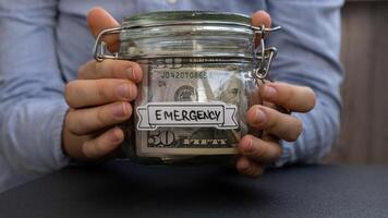 méconnaissable femme en portant verre pot plein de américain devise dollars en espèces billet de banque avec texte urgence. préparation économie argent. modérer consommation et économie. collecte argent photo