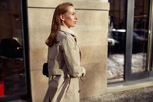 attrayant femme dans manteau traversée le ville rue et à la recherche à côté. flou Contexte photo