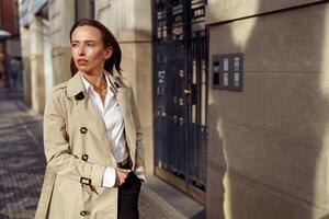 attrayant femme dans manteau traversée le ville rue et à la recherche à côté. flou Contexte photo