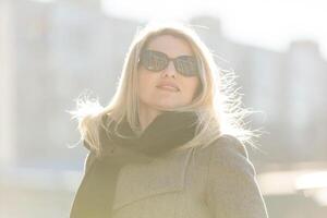 Jeune magnifique blond fille dans manteau avec une noir sac des promenades par le hiver et printemps ville photo