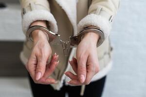 une femme qui a été arrêté et a sa mains menotté derrière sa retour à le arrière. le prisonnier est en attente transport à le prison. photo