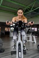 Jeune mignonne femme dans serré des sports costume formation sur exercice bicyclette dans Gym photo