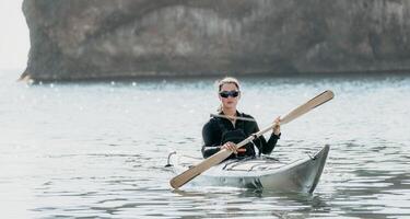 femme mer kayak. content souriant femme dans kayak sur océan, pagayer avec en bois rame. calme mer l'eau et horizon dans Contexte. actif mode de vie à mer. été vacances. photo