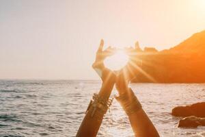 femme mer yoga. content femme dans blanc maillot de bain et boho style bracelets pratiquant en plein air sur yoga tapis par mer sur le coucher du soleil. femmes yoga aptitude routine. en bonne santé mode de vie, harmonie et méditation photo