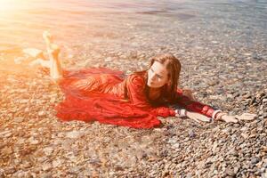 femme Voyage mer. content touristique dans rouge robe prendre plaisir prise image en plein air pour souvenirs. femme voyageur posant dans mer plage, entouré par volcanique montagnes, partage Voyage aventure périple photo