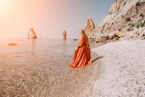 femme Voyage mer. content touristique dans rouge robe prendre plaisir prise image en plein air pour souvenirs. femme voyageur posant sur le Roche à mer baie entouré par volcanique montagnes, partage Voyage aventure périple photo