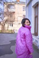 une élégant femme dans une longue brillant rose, magenta manteau et rouge des chaussures des promenades le des rues de le ville photo