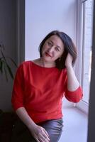 portrait de une brunette avec une bob la Coupe de cheveux dans une rouge chandail et une cuir mini jupe dans le Bureau photo