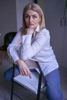 portrait de une blond femme dans jeans et une blanc chemise dans le Bureau photo