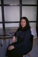 portrait de une moyen Taille femme avec noir cheveux dans une noir robe dans un Bureau photo